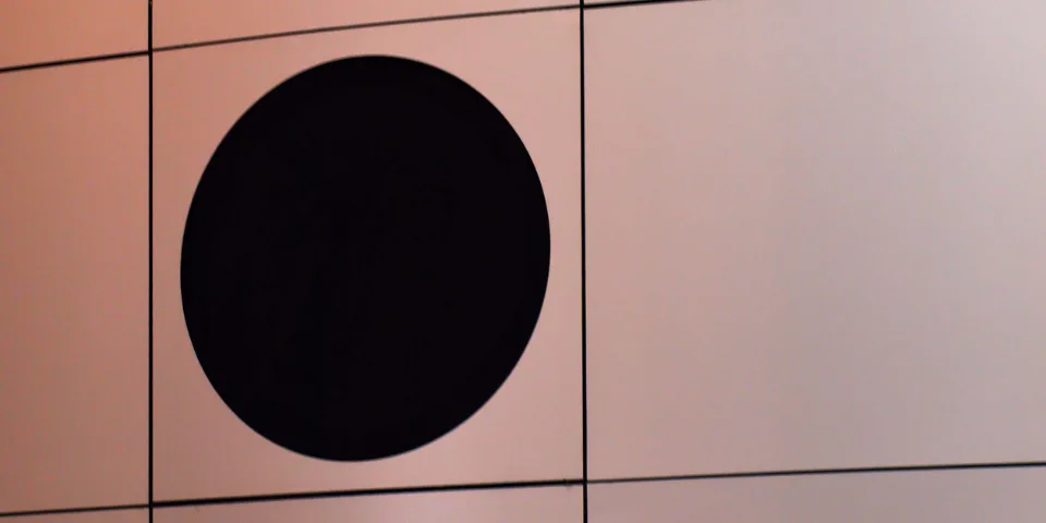 A wall of identical rectangular panels, with one panel holding a black circle that ignores the grid